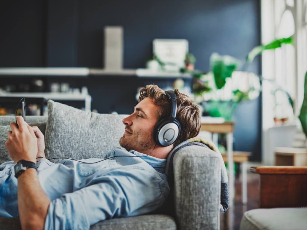 En mann slapper av på en sofa, lytter til musikk gjennom hodetelefoner, med et fredelig uttrykk i ansiktet